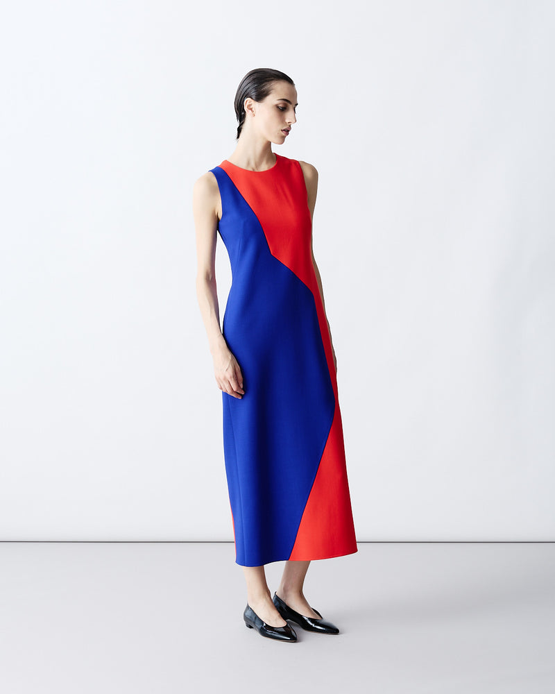 Detailed product shot of a sleeveless midi shift dress featuring a striking geometric blue and red color-block design. The dress is paired with black patent leather flats.