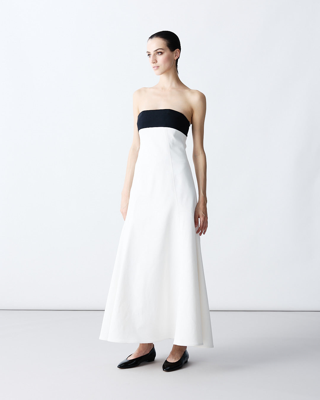 Minimalist two-tone evening gown: A strapless, floor-length dress with a striking black band bodice and a wide-sweeping white A-line skirt, set against a plain light studio background.