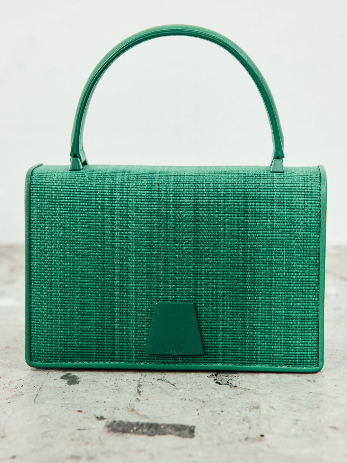 A structured emerald green handbag with a top handle, featuring a distinct woven texture and a clean, geometric clasp.