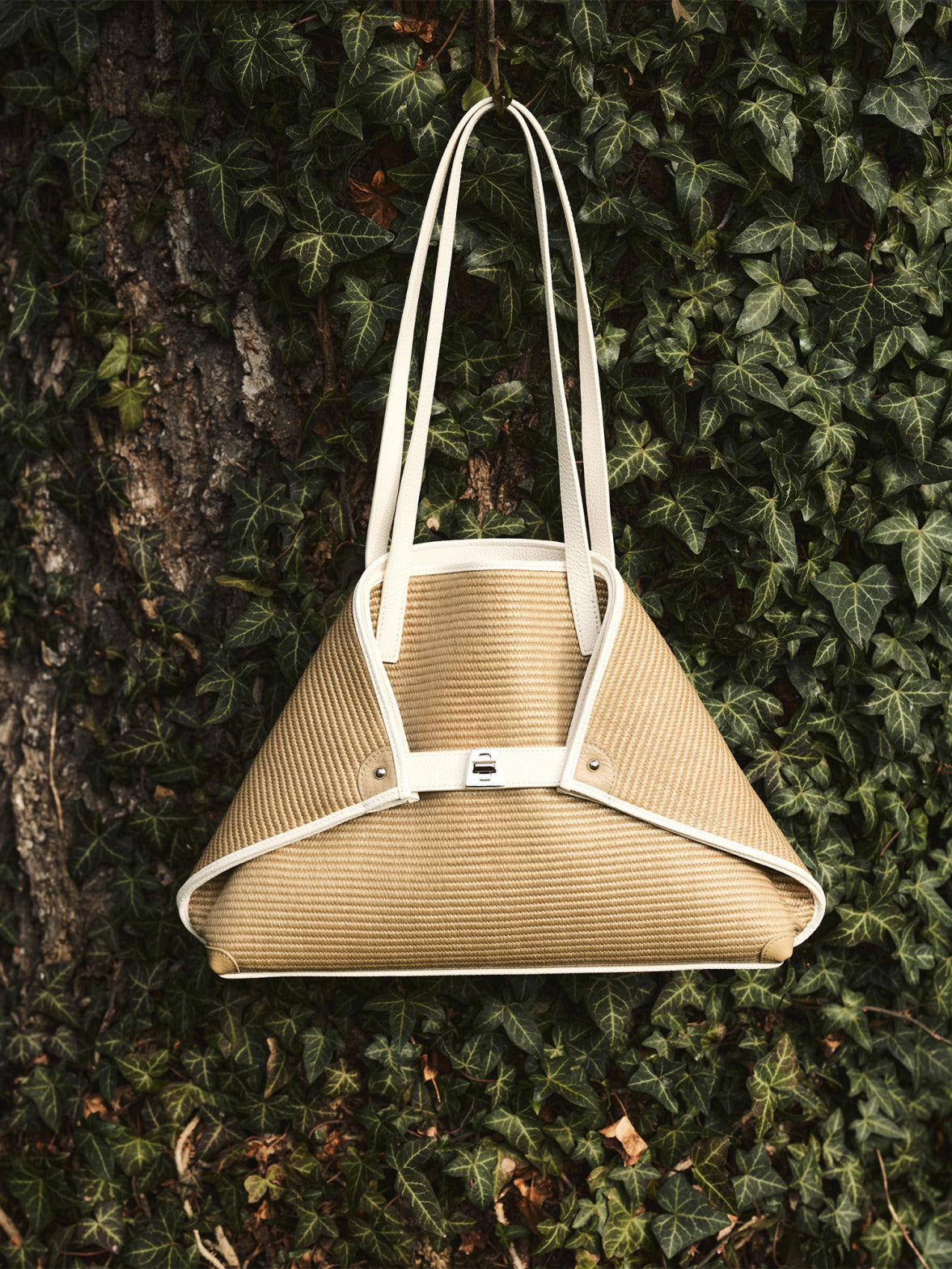 Akris woven raffia handbag with contrast white leather trim and straps.

Triangular designer tote from Akris, hanging from an ivy-covered tree.