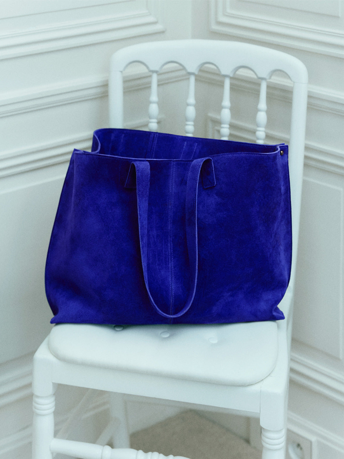 AI-generated vibrant royal blue suede tote bag on a white chair, luxury fashion concept.