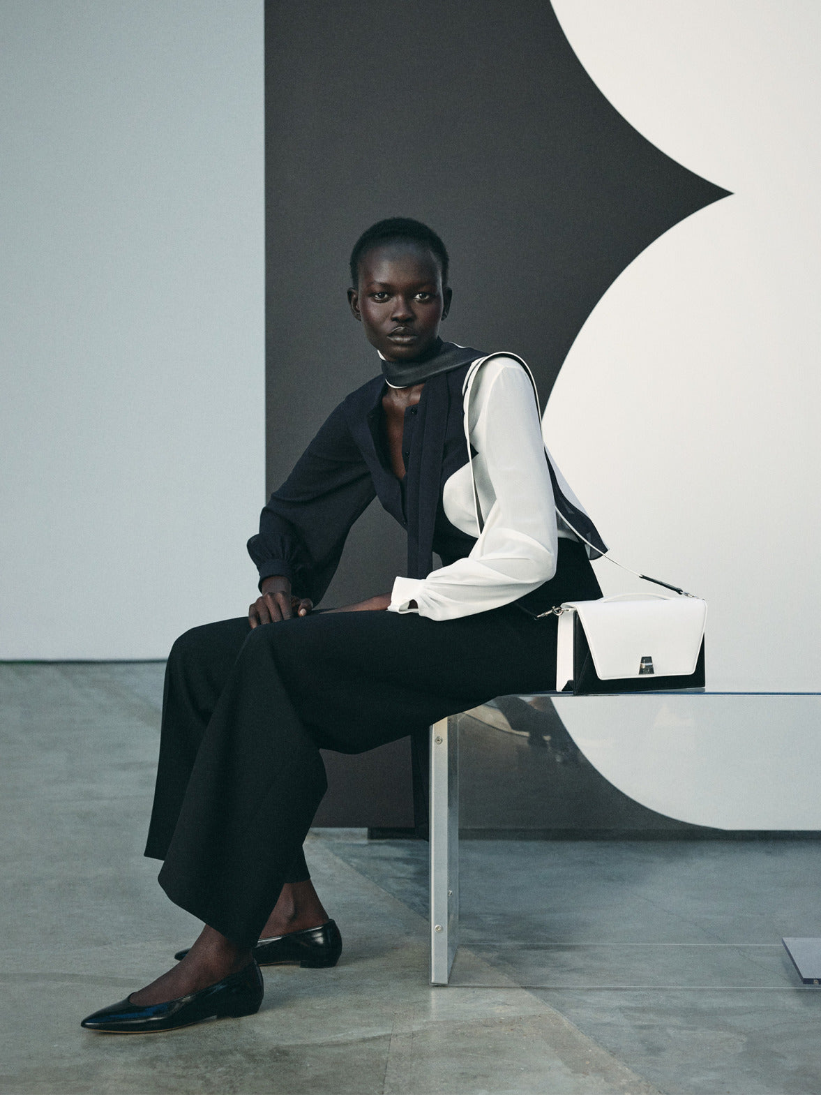 Akris Spring/Summer collection featuring a black and white tailored outfit with fluid blouse, wide-leg trousers, and structured leather shoulder bag, defined by minimalist elegance. Modern luxury with monochrome contrast, clean lines, and refined architectural tailoring.