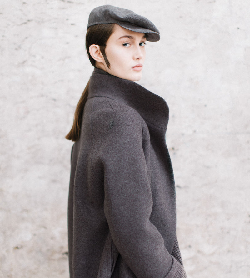 Model photographed sideways in a grey coat and matching beret.